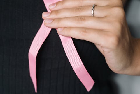 Close-up of a woman holding a pink ribbon, symbolizing breast cancer awareness.
