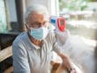Elderly man wearing a face mask having his temperature checked indoors with a contactless thermometer.