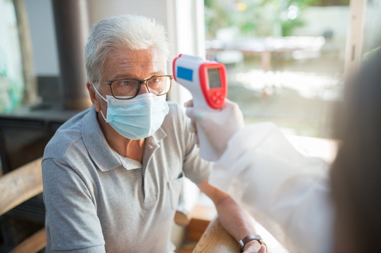Elderly man wearing a face mask having his temperature checked indoors with a contactless thermometer.