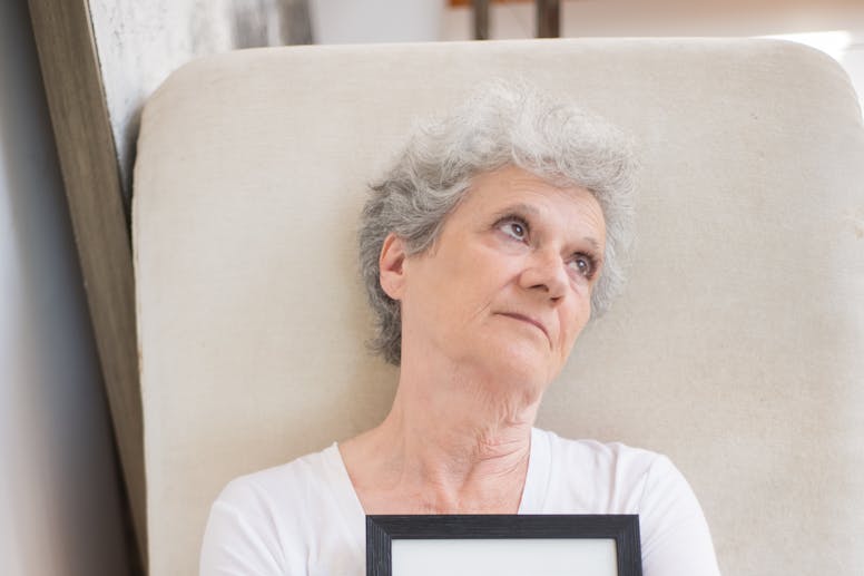 Elderly woman holding a framed photo, reflecting on memories and emotions.