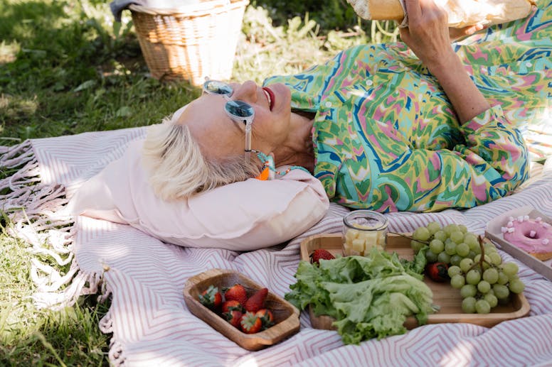 Elderly woman relaxing with picnic items on a sunny day, showcasing joy and leisure.