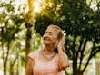 Graceful senior woman in a pink dress enjoying a peaceful moment outdoors amidst sunlit trees.