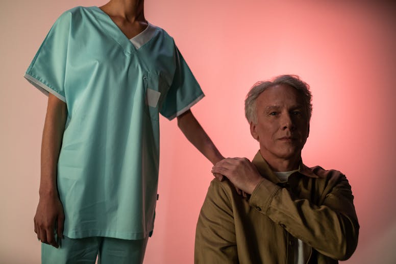 Portrait of an elderly man with a caregiver in medical attire, studio light background.