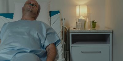 A man lying in a hospital bed with a nasal cannula, illuminated by bedside lamp.